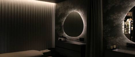 A modern bathroom with a bench, a round mirror, and a textured wall.