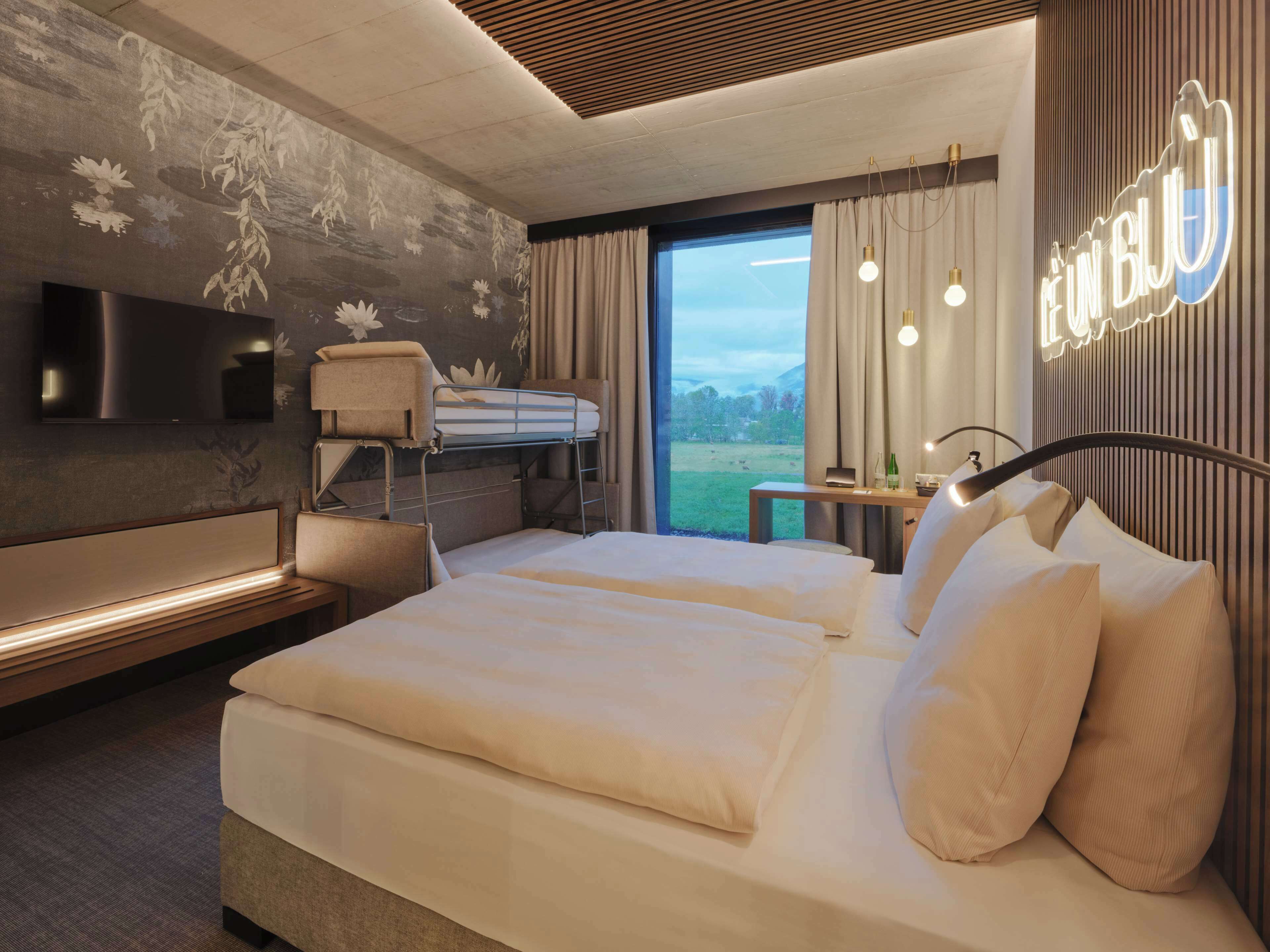 Una habitación de hotel moderna con una cama grande, un escritorio, un televisor y vistas al exterior.