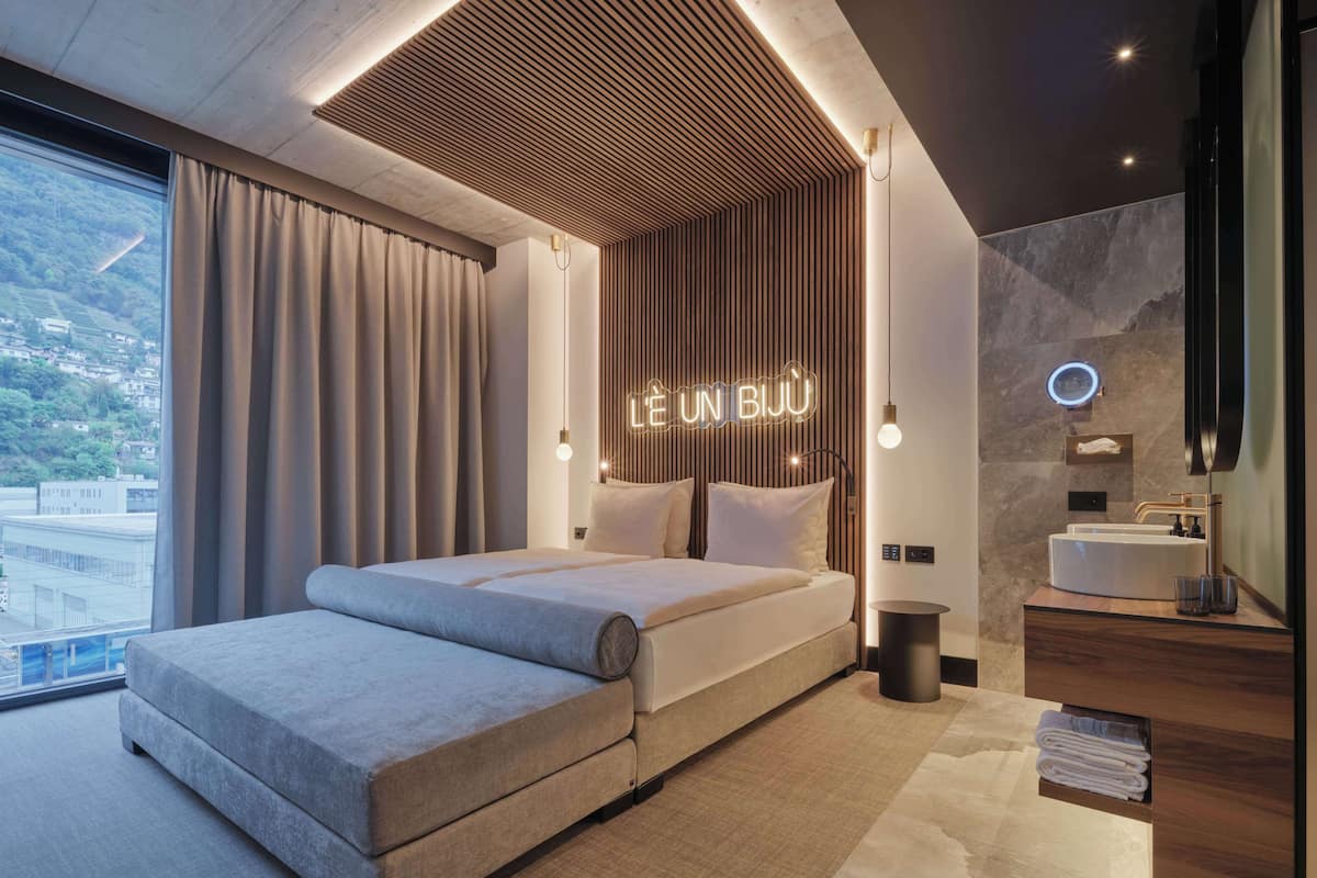A modern hotel room with a large bed, a bathroom with a vanity, and a view of the city.