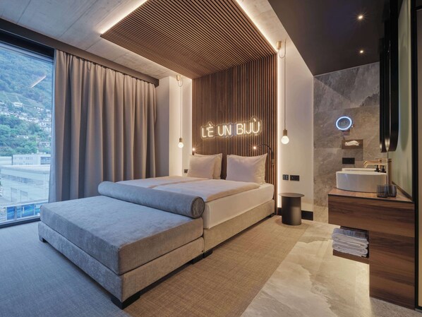 A modern hotel room with a large bed, a bathroom with a vanity, and a view of the city.