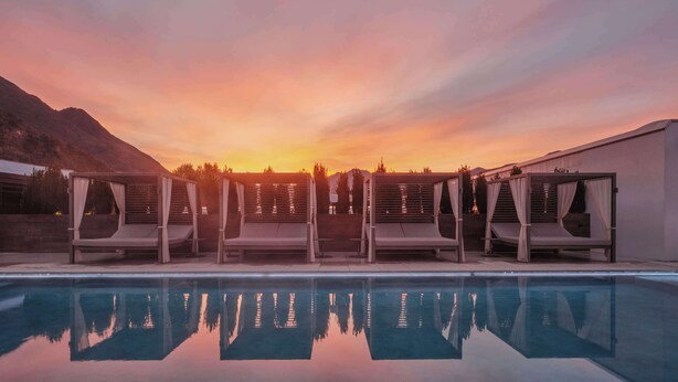A poolside area with lounge chairs and a clear view of the sunset over mountains. - Dorint Resort & Spa Locarno Riazzino (Locarno)