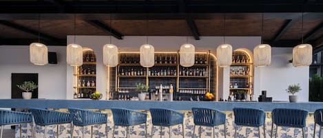 An outdoor bar area with blue chairs, a tiled floor, and a bar stocked with bottles.