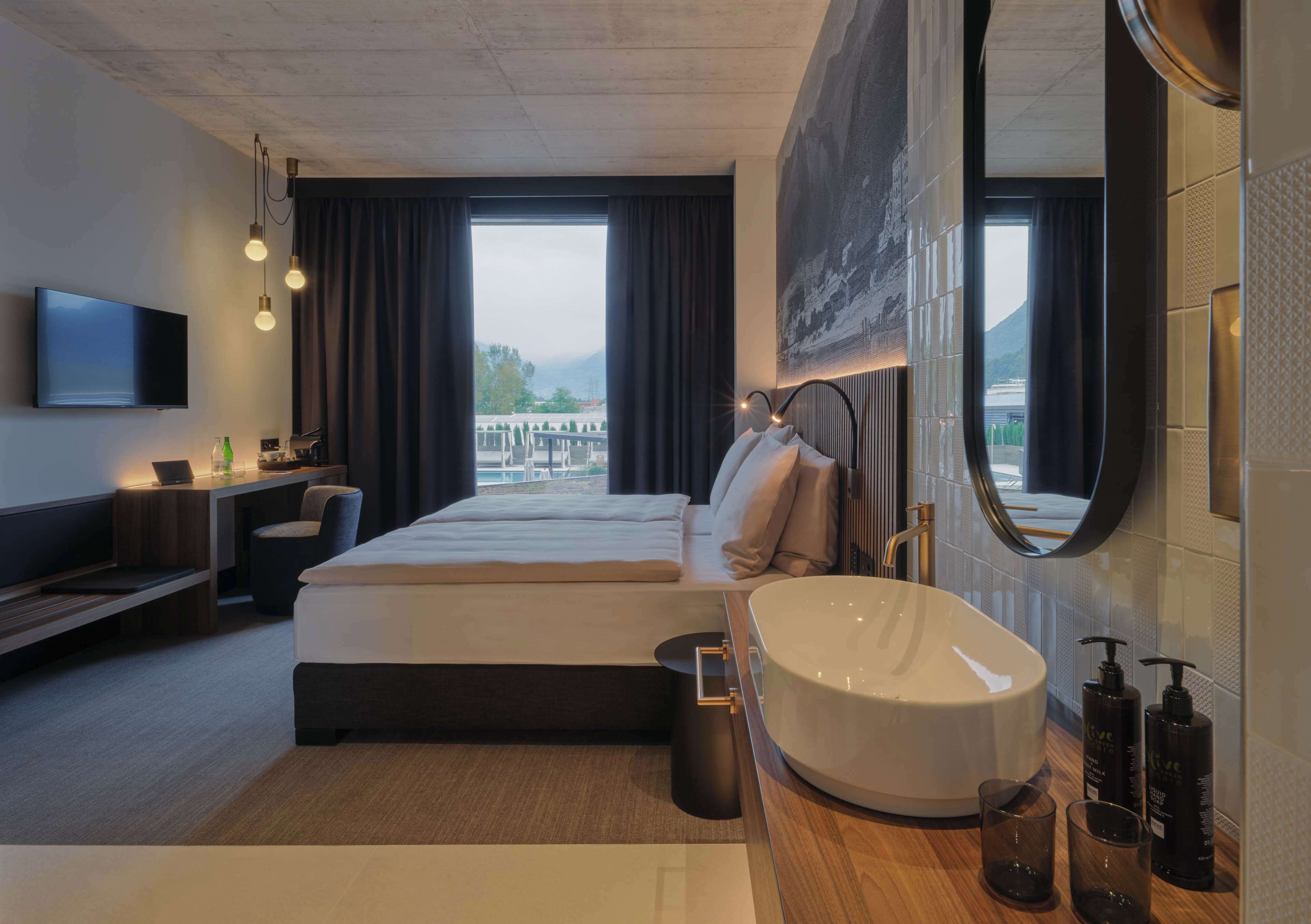 Quarto de hotel moderno com cama grande, banheira redonda, televisão de tela plana e vista para as montanhas.