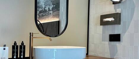 Un baño moderno con un lavamanos blanco redondo, un espejo grande y un dispensador de toallas.