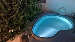 A swimming pool with a unique shape, surrounded by a low wall and some greenery. - Dar Essaroual Hammamet (Hammamet)