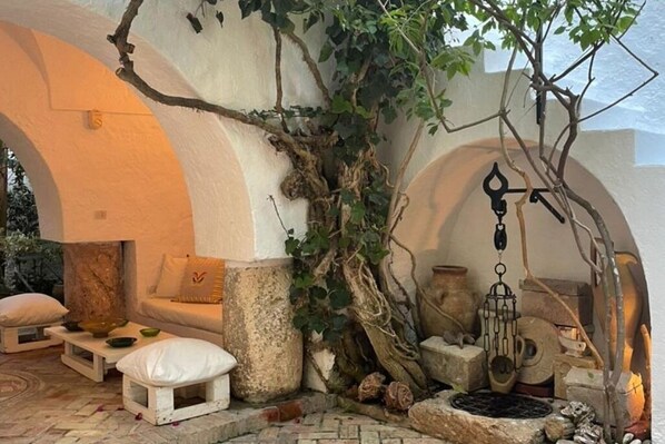 Un espacio al aire libre acogedor con un banco de piedra, cojines y una pequeña mesa.