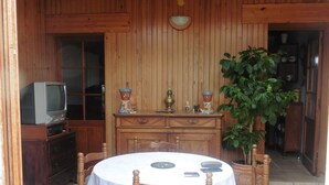 Un interior de fusta amb taula de dinar, cadires, televisor i una planta en test.