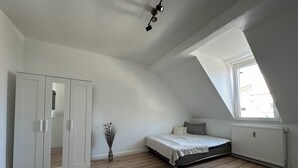 A bedroom with a sloped ceiling, a bed, a wardrobe, and a window. - Zentrales Neues, Modernes Apartment. Schneller Zugang Mittels Code-schloss (Herne)