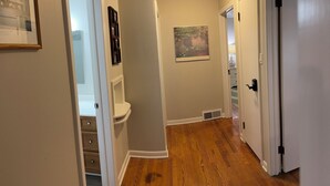 A hallway with wooden flooring, white walls, and a ceiling light. There are framed pictures on the walls and a door on the right. - Durham Vacation or Work Rental (Durham)