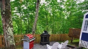 Un jardin avec un barbecue, une lanterne noire et deux chaises de jardin blanches.