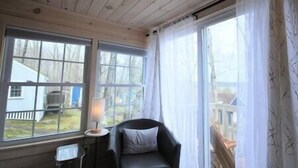 Une pièce avec un plafond en bois, une chaise avec un coussin, une table avec une lampe et de grandes fenêtres avec des rideaux.
