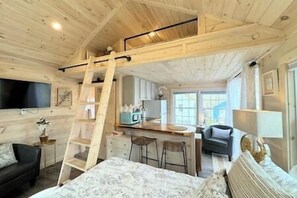 A wooden cabin interior with a loft bedroom, a kitchen area, and a dining space. - Cheerful Cottage with Loft 9 (Edgecomb)