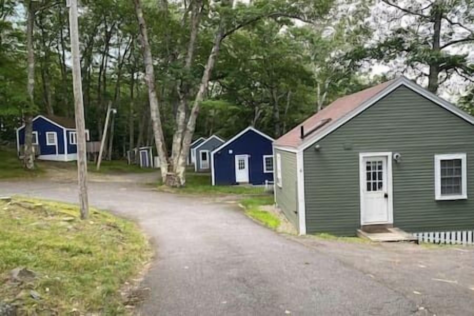 Une rangée de cabanes, avec un chemin de gravier menant à elles, le tout entouré d’arbres.