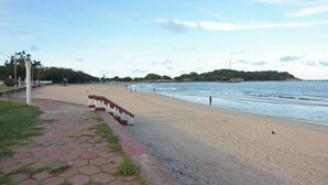 A beach with a paved walkway, a fence, and a distant island. - Trinco Rest House (Trincomalee)