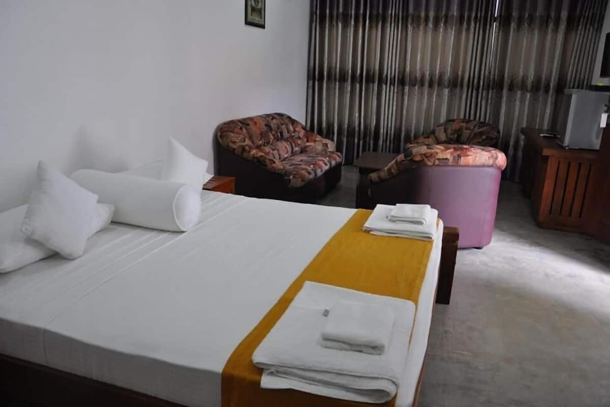 A hotel room with a bed, two armchairs, a small table, and a television.