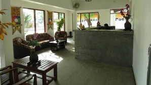 A spacious living area with a sofa, coffee table, and a dining table. There is a kitchen area with a counter and a hanging light fixture. - Trinco Rest House (Trincomalee)