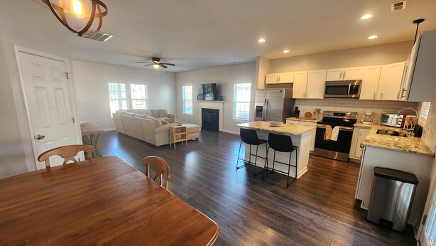 A spacious living area with a wooden dining table, a sofa, and a kitchen with modern appliances.