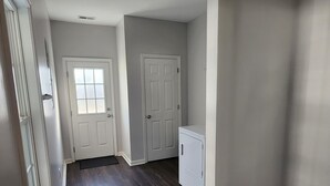 A hallway with two white doors, a small white laundry machine, and a dark wooden floor.