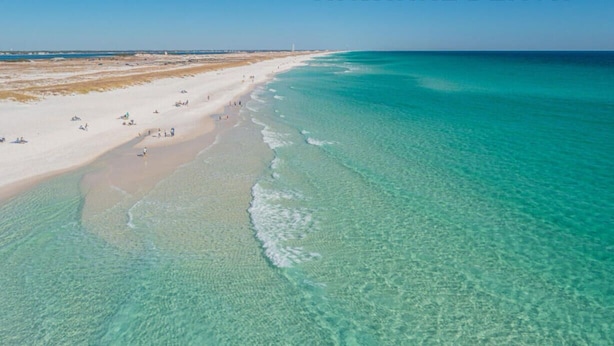 Luchtbeeld van een strand met helder turquoise water en een zandstrand.