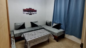 Una habitación con sofá cama, una mesita, un cuadro en la pared y una cortina azul.