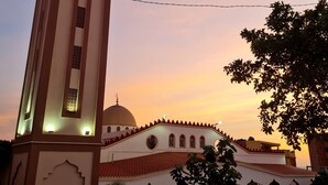 Un edificio con una torre y una cúpula destacadas, rodeado de árboles y un cielo despejado.