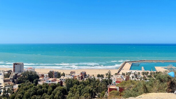 Un pueblo costero con playa, puerto deportivo y edificios en primer plano.