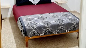 Un dormitorio con cama, mesita de noche, lámpara de pared y una pequeña estantería.