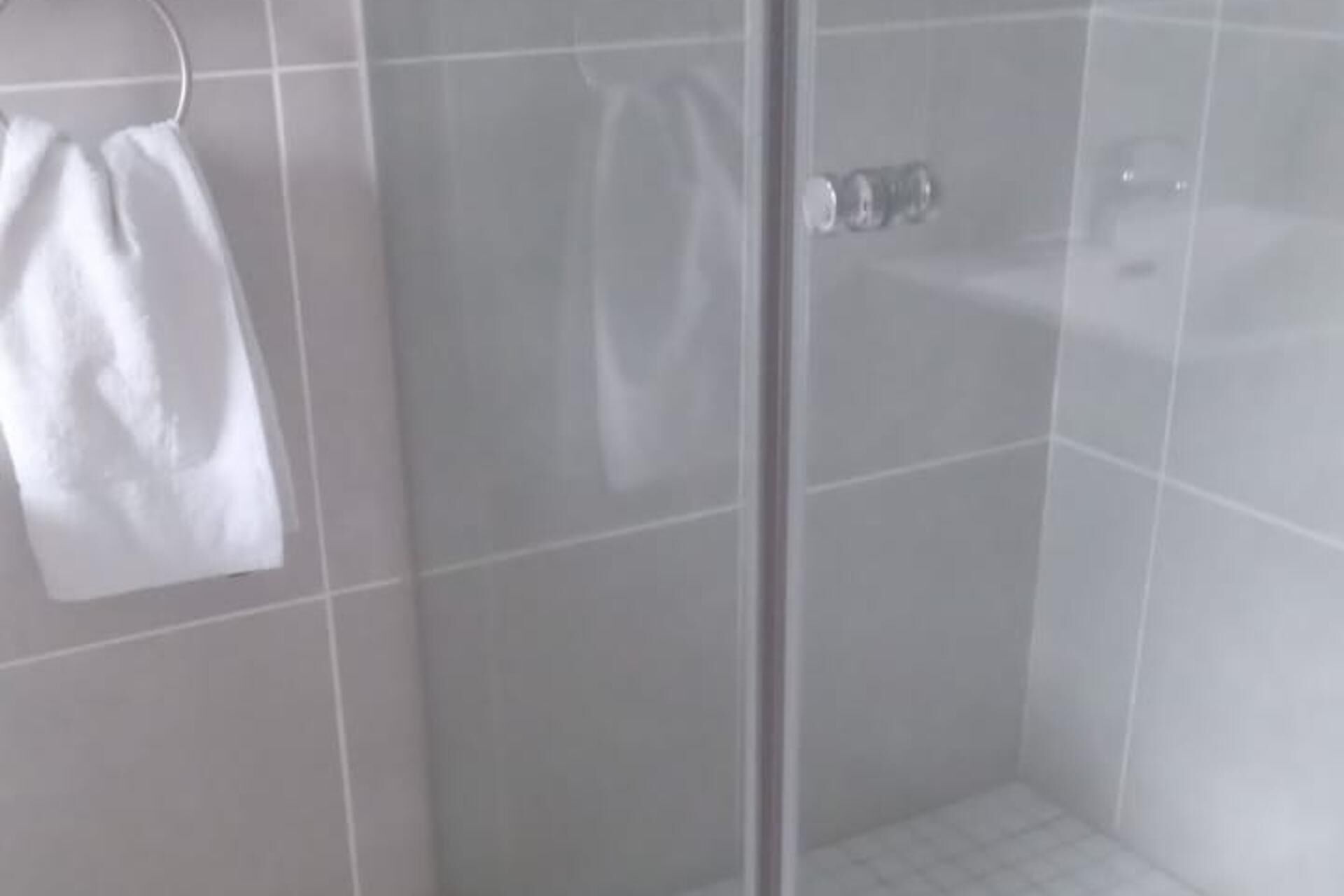 A bathroom with a glass shower enclosure, a towel rack, and a tiled floor.