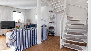 A modern living room with a sofa, TV, and a white staircase. - Semesterboende på Öland (Kalmar län)