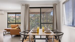A dining area with a table set for two, a sofa, and a view of a natural landscape through large windows. - NorthStar 2, perfectly situated in the heart of Jindabyne (Jindabyne)