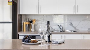 A kitchen counter with a bottle of wine, two wine glasses, a plate with grapes, and a cloth napkin. - NorthStar 2, perfectly situated in the heart of Jindabyne (Jindabyne)