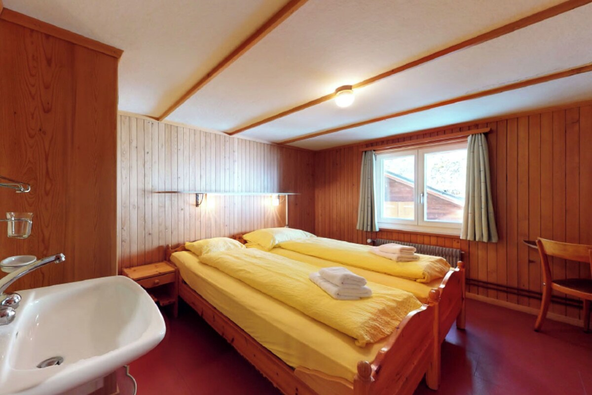 A wooden room with two beds, a sink, and a window with curtains.