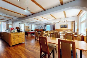 A spacious dining area with wooden tables and chairs, a central pool table, and a kitchen area with a refrigerator and sink. - Gadmen Alpenrose Switzerland (Innertkirchen)