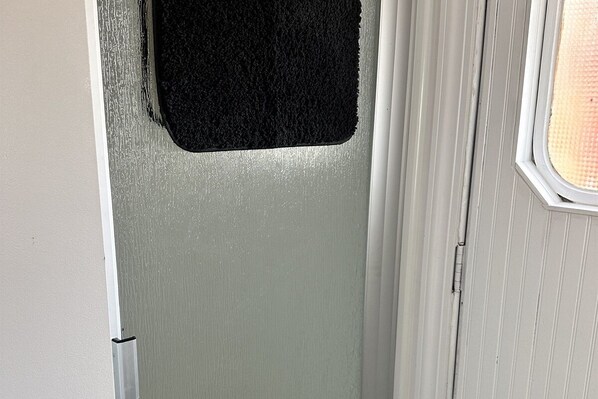 Una puerta con felpudo negro y una ventana con persiana texturizada.