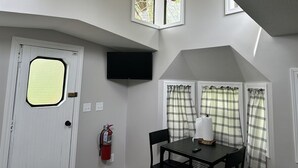 A room with a door, a fire extinguisher, a table with chairs, and a television mounted on the wall.