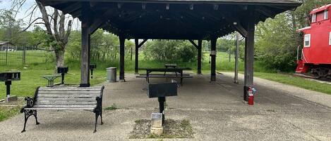 Un kiosque agrémenté de bancs et de tables de pique-nique, situé dans un parc.