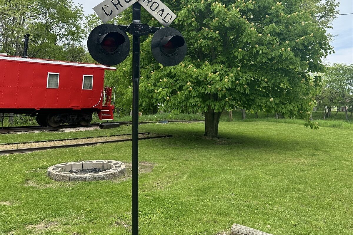 A railroad crossing with a red train car and a 'CROSSING' sign.