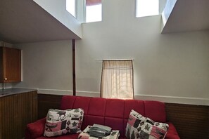 Un canapé rouge avec des coussins à motifs, un meuble en bois et une fenêtre avec un rideau.