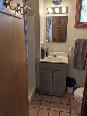 Un bagno con un mobile bagno in legno, un lavandino, uno specchio e una tenda da doccia.