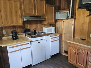 A compact kitchen with wooden cabinets, a microwave, a coffee maker, and a small refrigerator.