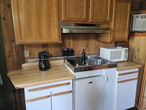 A compact kitchen with wooden cabinets, a coffee maker, a microwave, and a refrigerator.