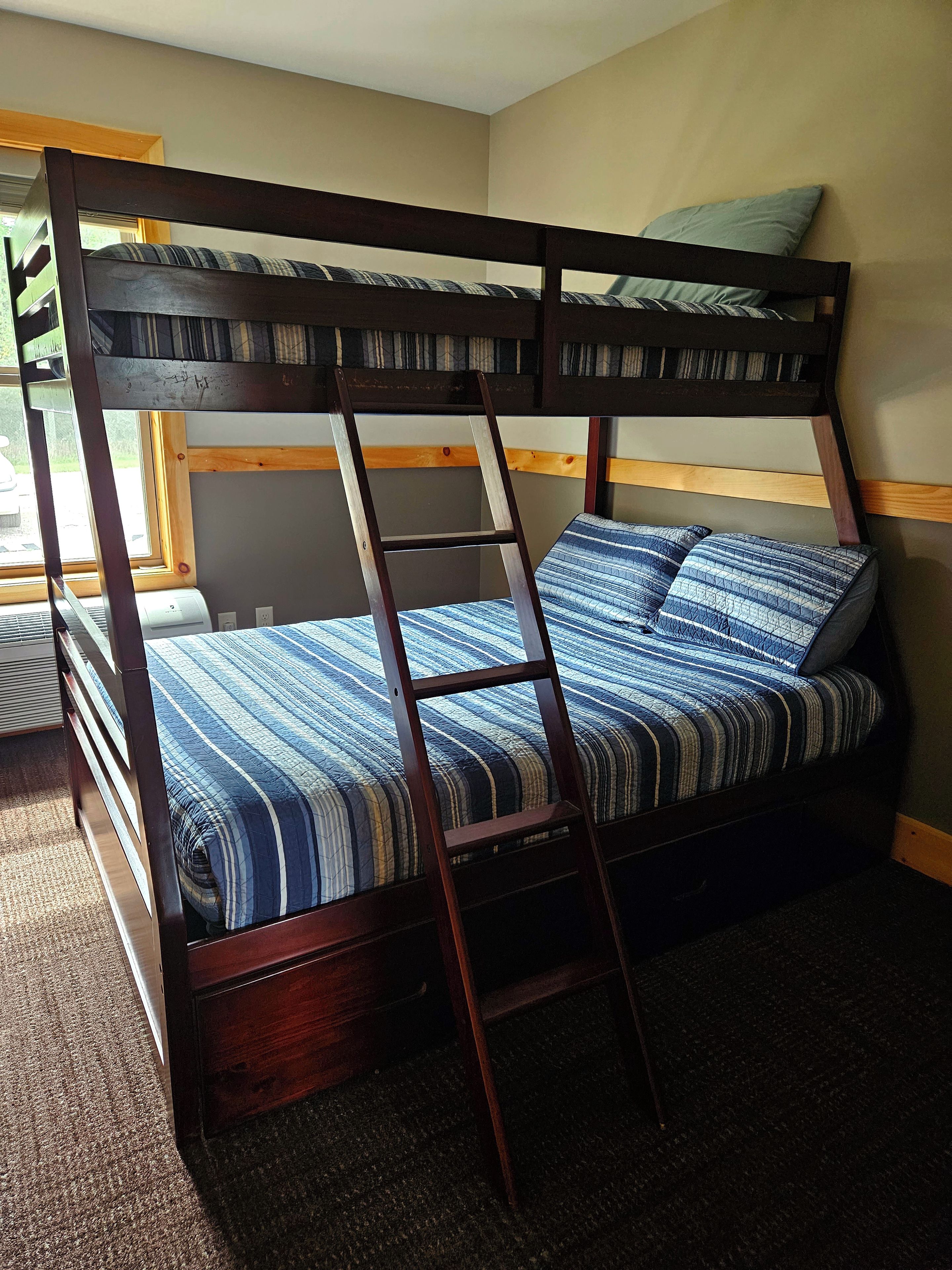 A bunk bed with a ladder, a window with blinds, and a carpeted floor.