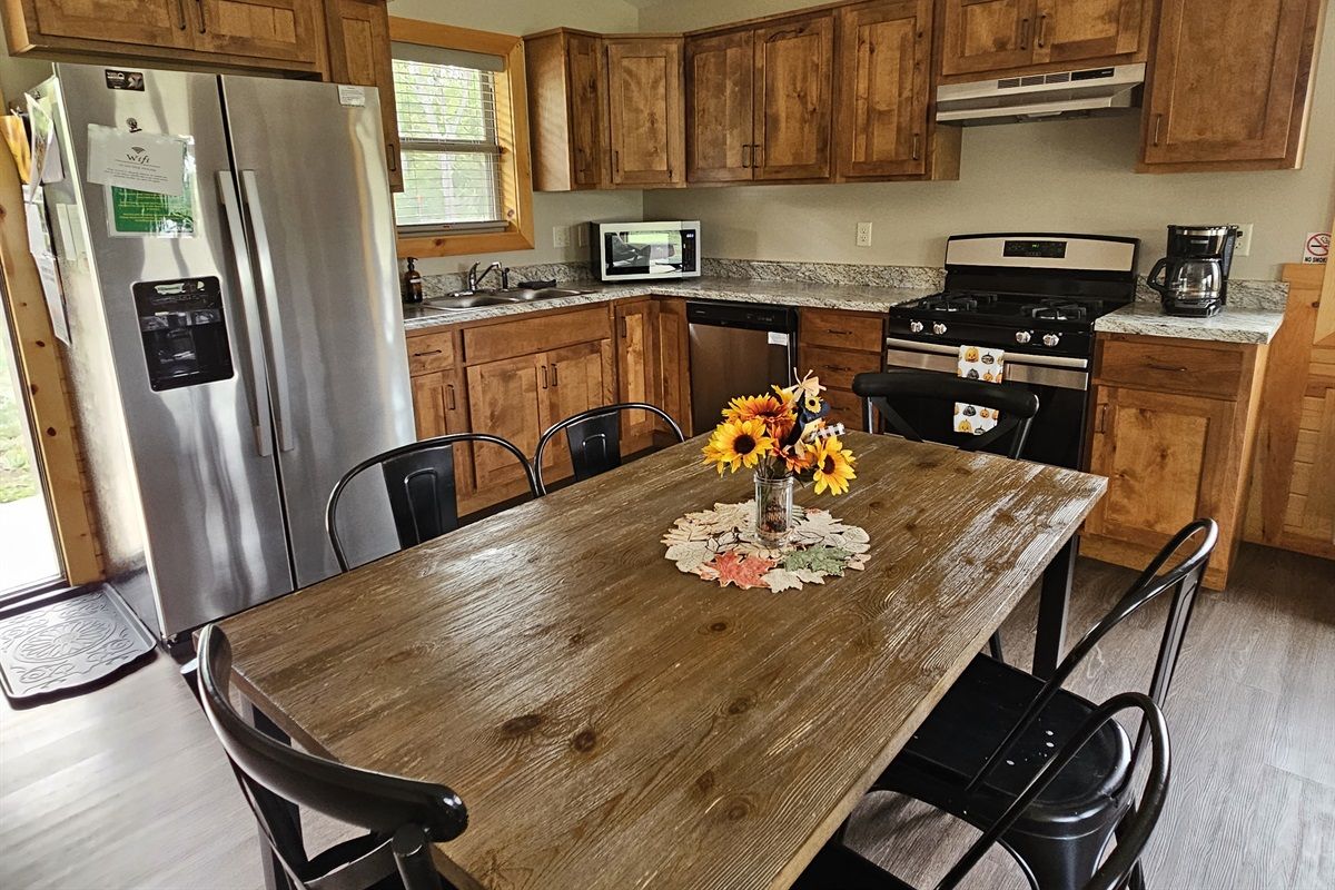 A kitchen with wooden cabinets, a stainless steel refrigerator, a microwave, a stove, and a dining table with chairs.
