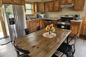 Une cuisine avec des meubles de rangement en bois, un réfrigérateur en acier inoxydable, un four à micro-ondes, une cuisinière et une table à manger avec des chaises.
