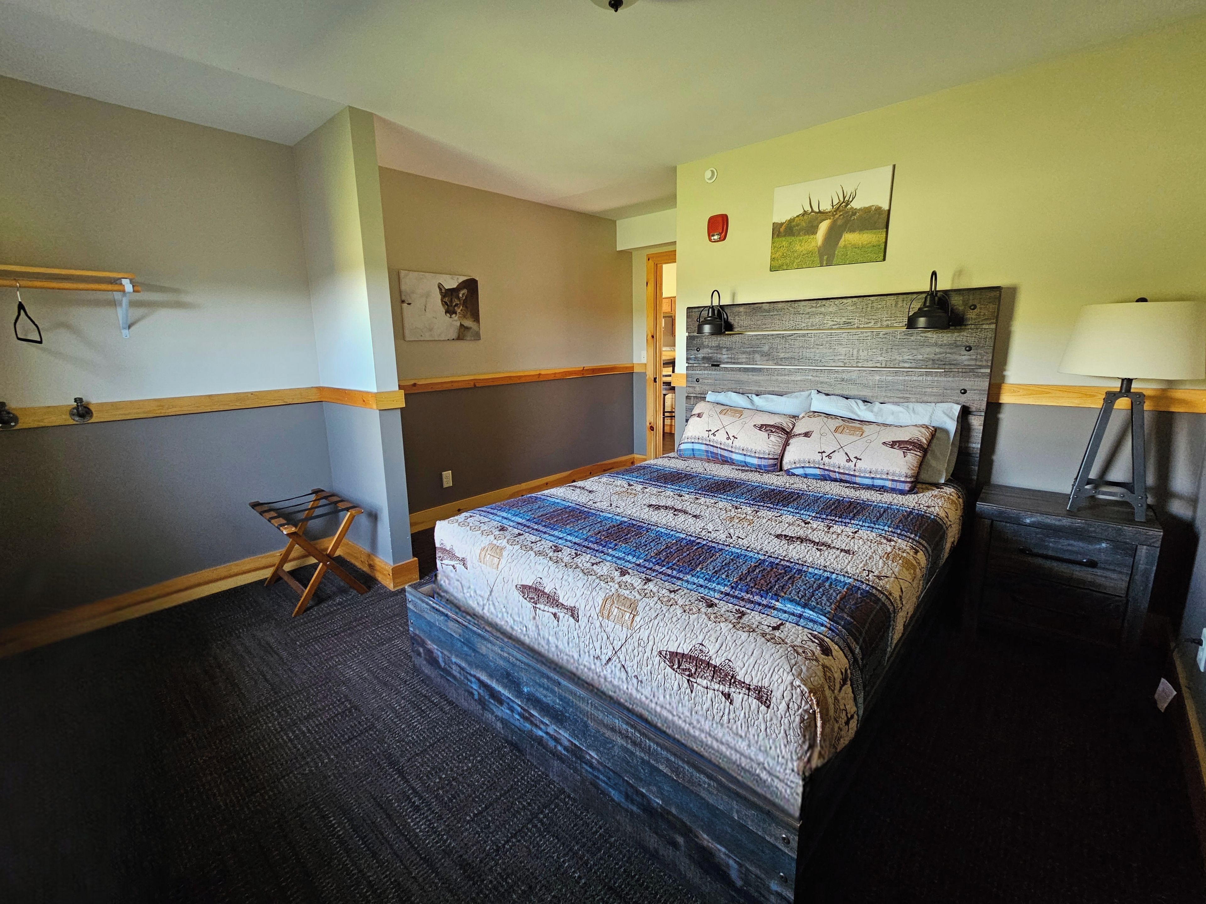 Une chambre d’hôtel avec un lit, des tables de chevet, une étagère fixée au mur, une porte et un tableau accroché au mur.