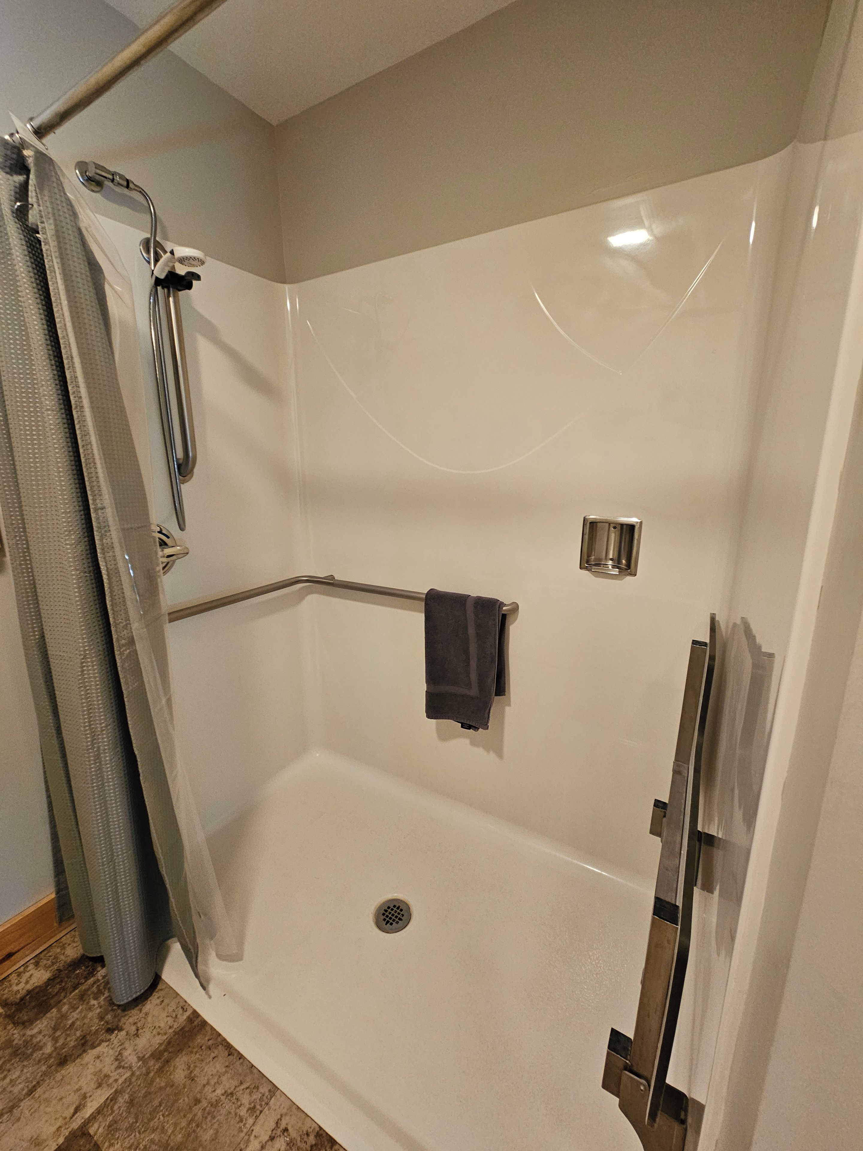A walk-in shower with a glass door, a handheld showerhead, a towel rack, and a shower control panel.