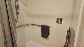A walk-in shower with a glass door, a handheld showerhead, a towel rack, and a shower control panel.