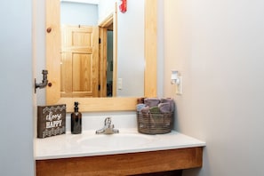 A bathroom with a wooden vanity, a mirror, a sink, a soap dispenser, and a towel basket.