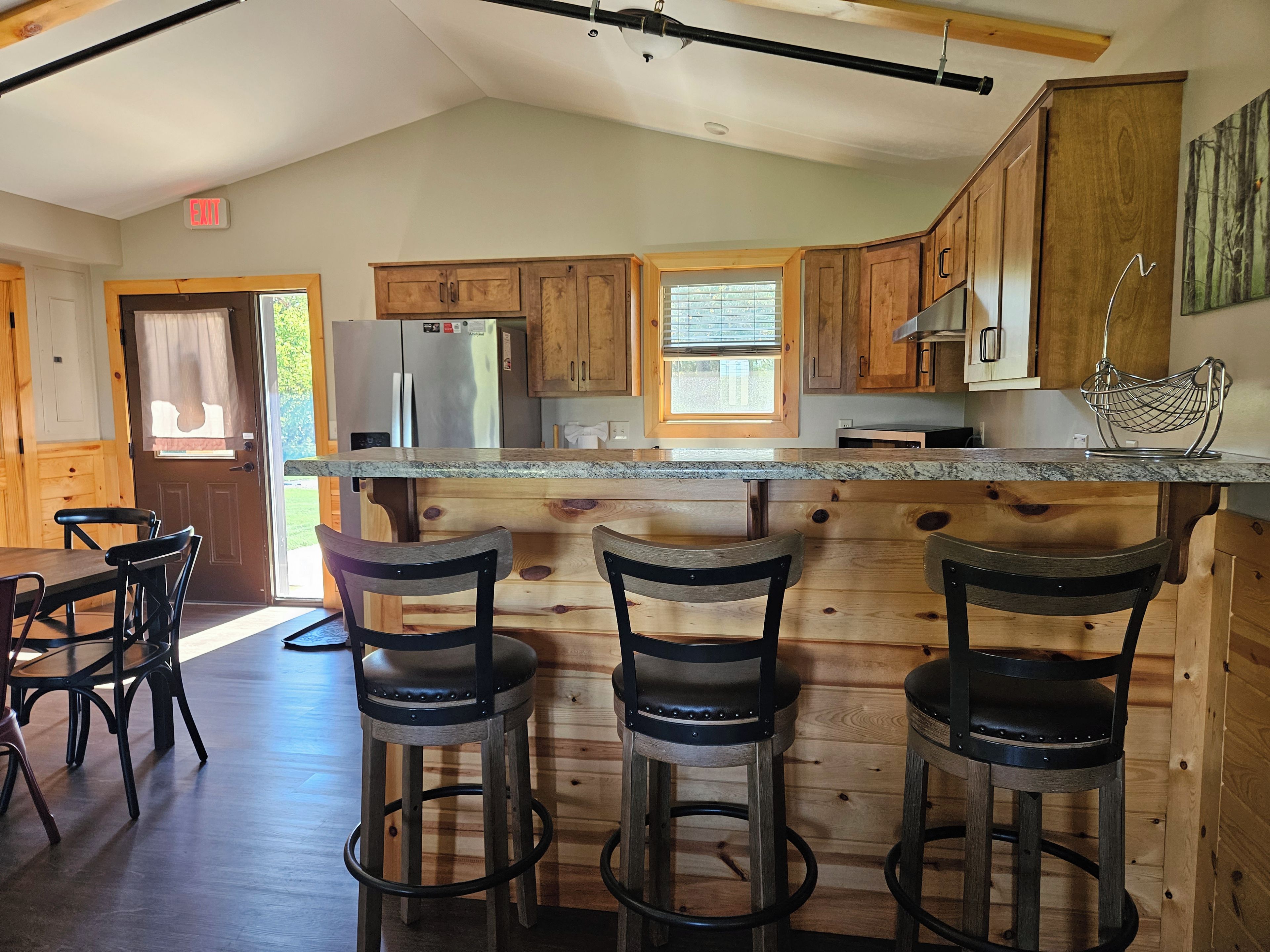A kitchen with wooden cabinets, a stainless steel refrigerator, a marble countertop, and bar stools.