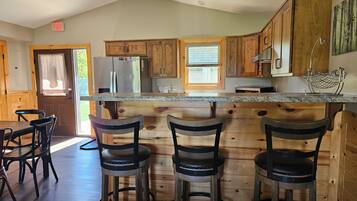 A kitchen with wooden cabinets, a stainless steel refrigerator, a marble countertop, and bar stools.
